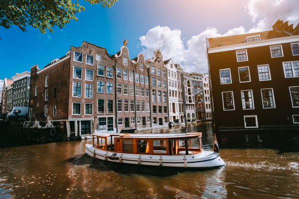City of Amsterdam in Holland picturesque scenery, white boats on a canal between historic houses August - lunch boat trip